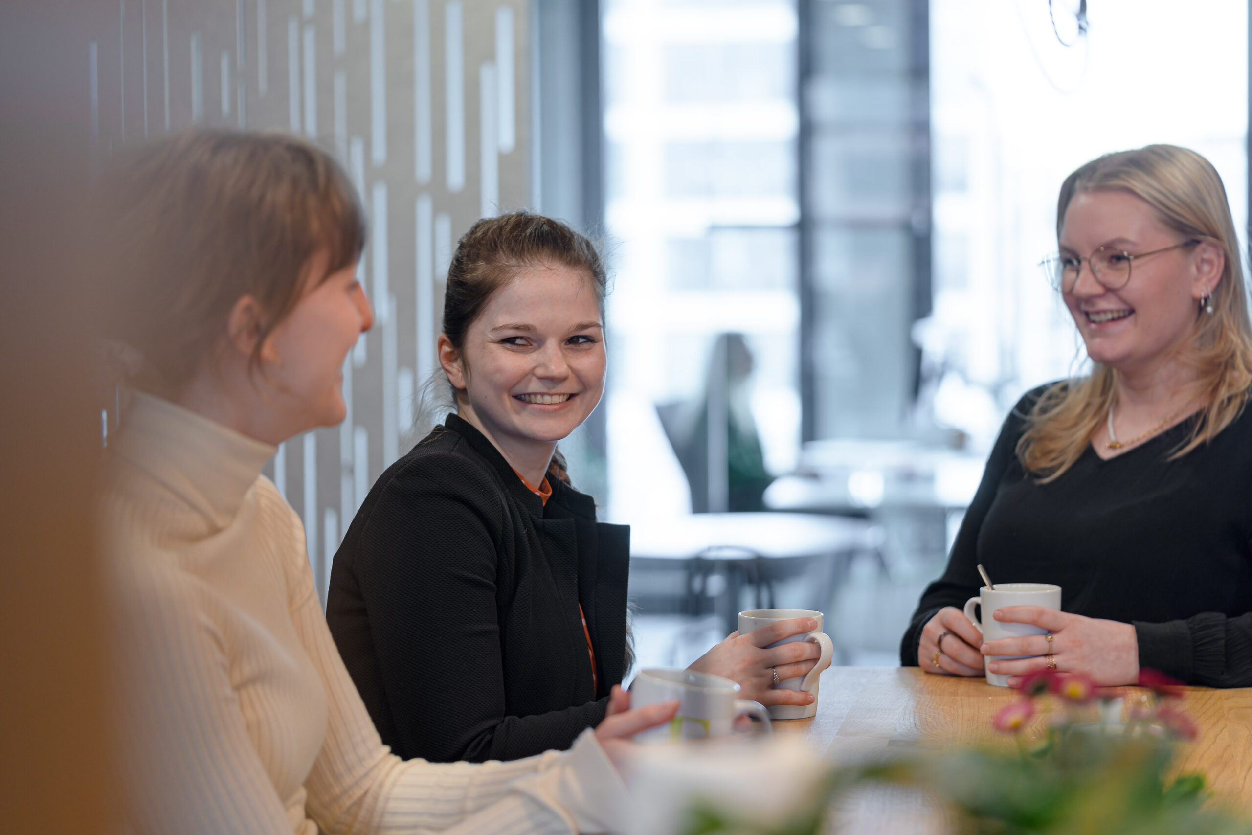 Drei junge Frauen unterhalten sich bei Kaffee am Konferenztisch