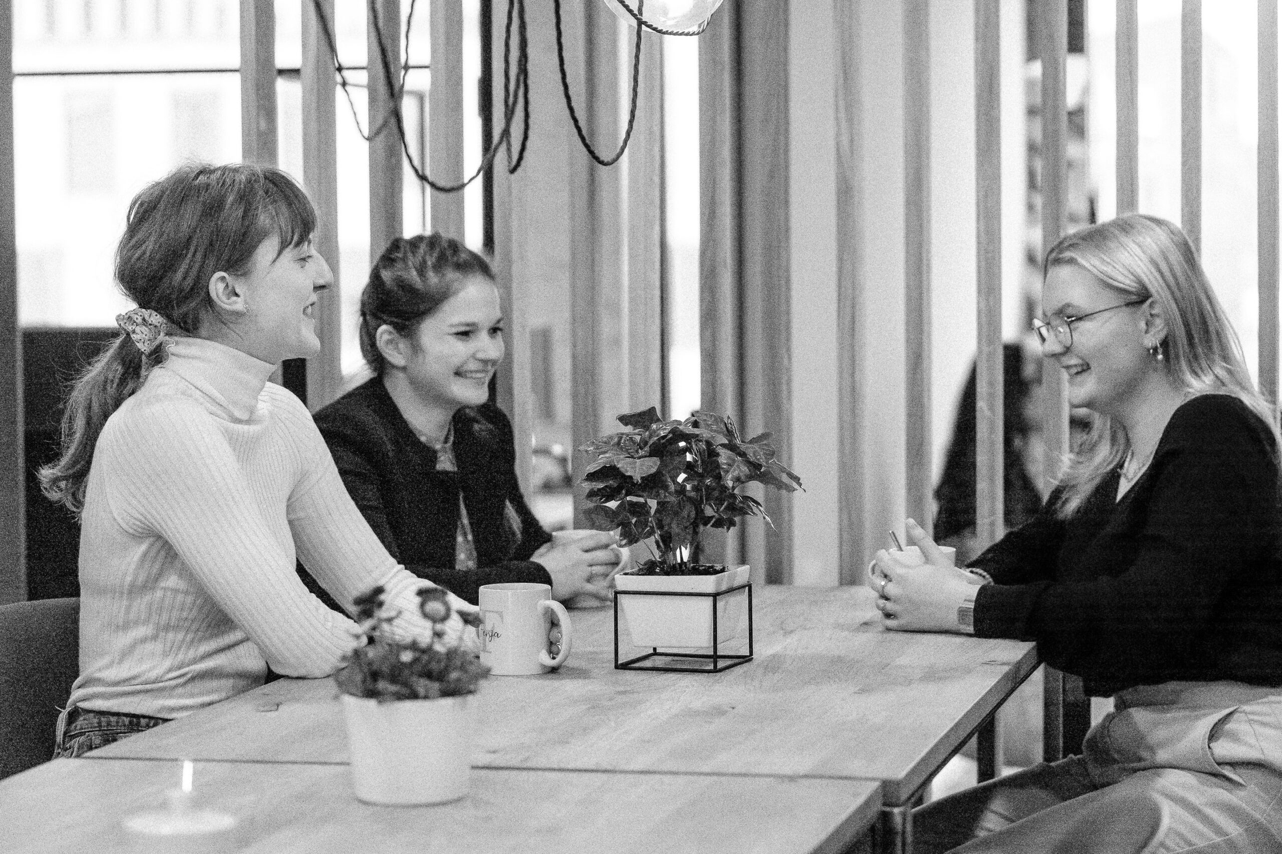 Drei junge Frauen beim Gespräch am Konferenztisch lachen